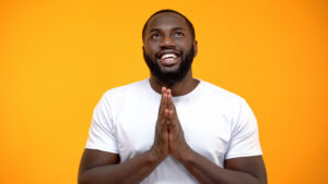 A person looking up and smiling with hands together in prayer position.